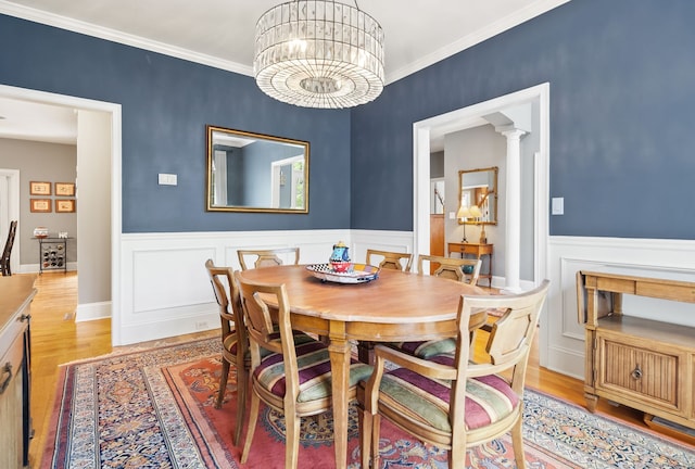 dining area featuring light wood-style floors, wainscoting, a chandelier, crown molding, and decorative columns