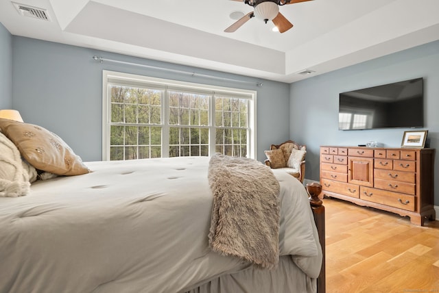 bedroom with a raised ceiling, light wood-style floors, and a ceiling fan