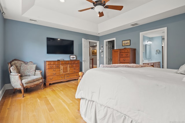 bedroom with a tray ceiling, light wood-style flooring, connected bathroom, and baseboards