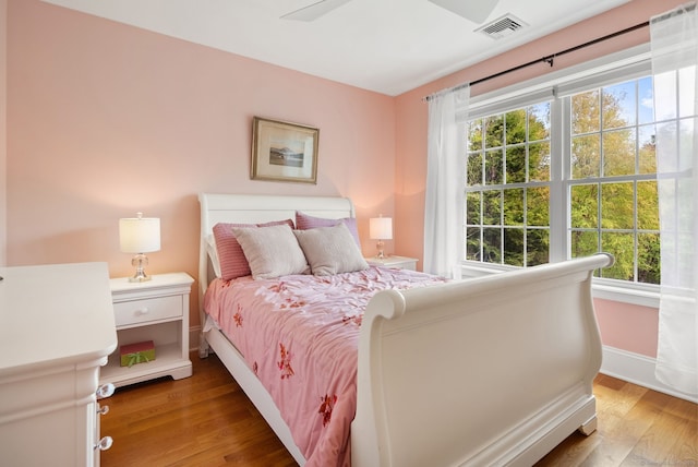 bedroom with multiple windows, wood finished floors, and baseboards