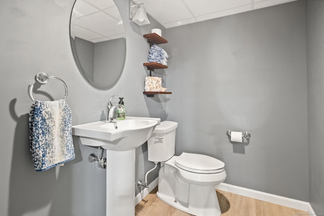 bathroom with a drop ceiling, wood finished floors, toilet, and baseboards