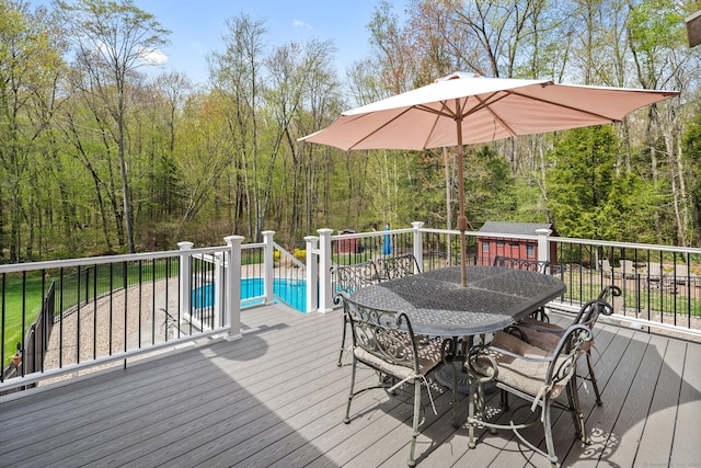 wooden deck featuring outdoor dining space, a wooded view, an outdoor structure, and a storage shed