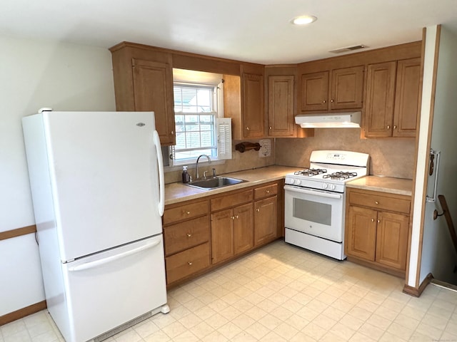 kitchen featuring white appliances, light countertops, under cabinet range hood, brown cabinets, and a sink