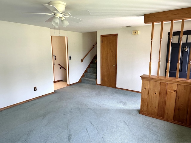 carpeted empty room featuring baseboards, a ceiling fan, and stairs