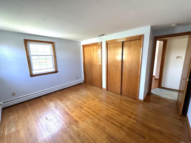 unfurnished bedroom featuring baseboard heating, multiple closets, baseboards, wood finished floors, and visible vents