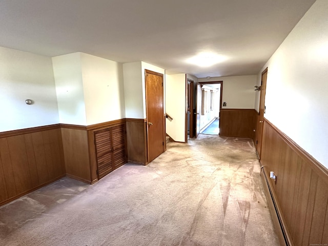 corridor with a baseboard radiator, light carpet, wainscoting, and wood walls