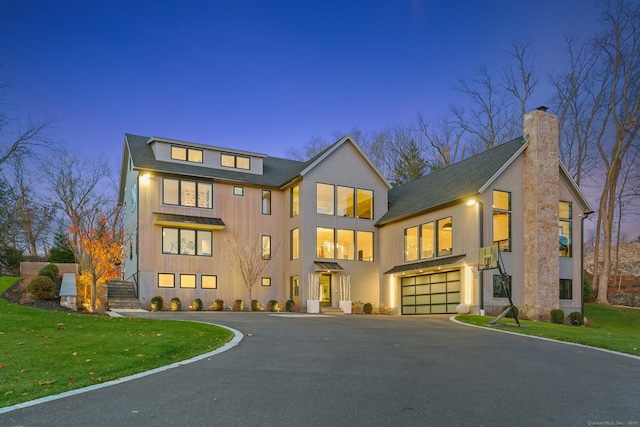 modern home with a chimney, roof with shingles, a front yard, a garage, and aphalt driveway