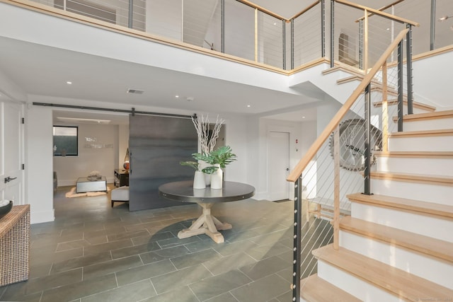 staircase featuring visible vents, a barn door, baseboards, tile patterned floors, and a high ceiling