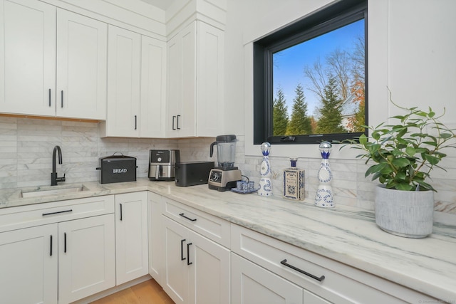 kitchen with a sink, light stone counters, backsplash, and white cabinetry
