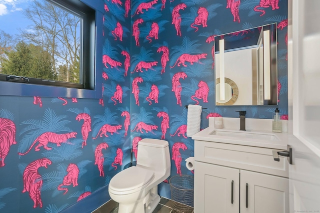 bathroom with vanity, toilet, and wallpapered walls