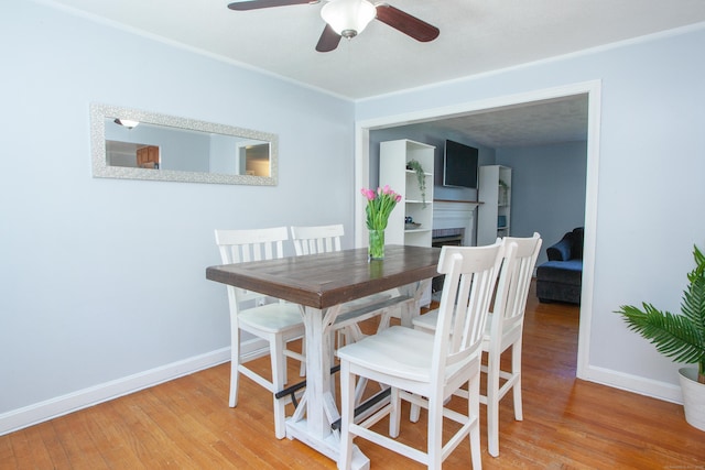 dining area with baseboards, ceiling fan, wood finished floors, and a fireplace
