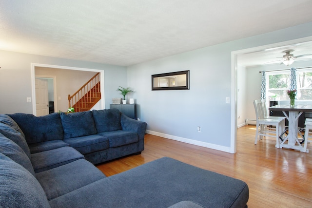 living area with baseboards, a ceiling fan, stairs, and light wood-style flooring