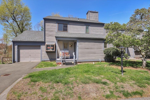 traditional-style house with a chimney, roof with shingles, a front yard, aphalt driveway, and an attached garage