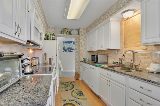 kitchen with white appliances, white cabinetry, a sink, and backsplash