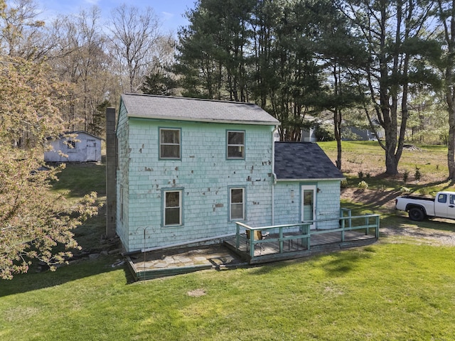 back of property with a lawn, a shingled roof, and a deck