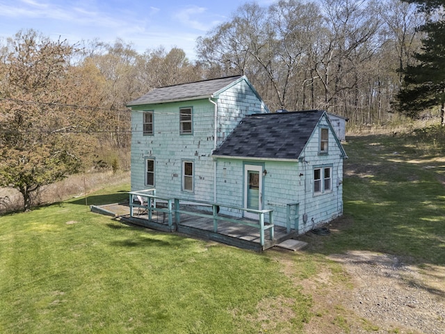 rear view of house with roof with shingles, a wooden deck, and a yard