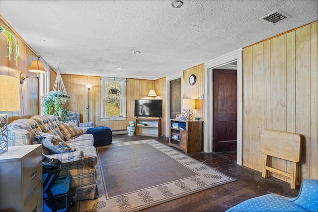 living room with a textured ceiling, visible vents, a baseboard heating unit, wooden walls, and hardwood / wood-style floors