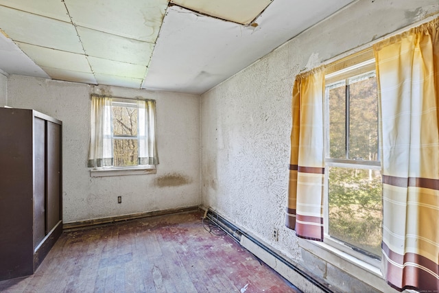 empty room featuring a textured wall, baseboard heating, and hardwood / wood-style floors
