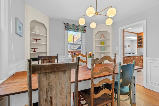 dining area featuring light wood-style flooring, a decorative wall, wainscoting, and built in shelves