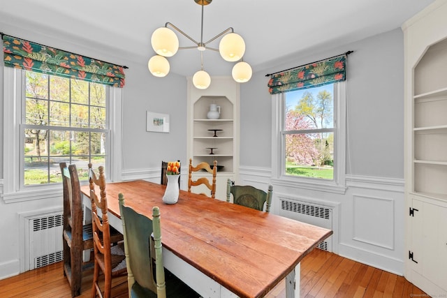 dining room with radiator, light wood finished floors, built in features, and a healthy amount of sunlight