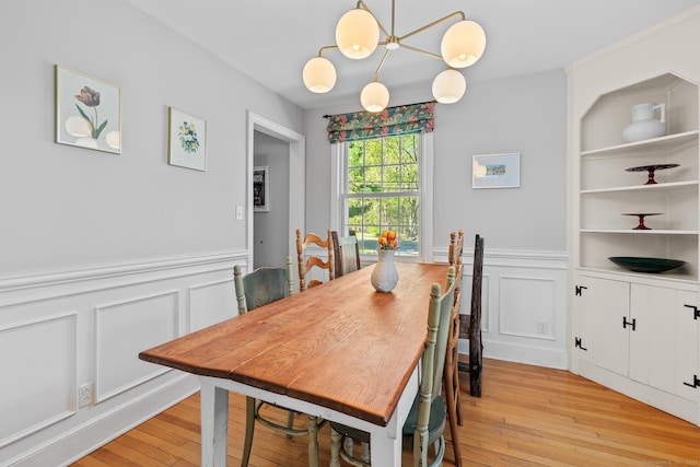 dining space featuring light wood-style floors, built in features, a wainscoted wall, and a decorative wall
