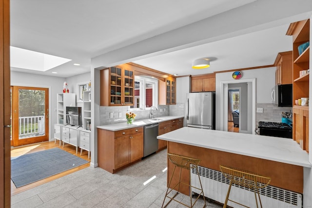 kitchen featuring open shelves, a peninsula, radiator heating unit, light countertops, and appliances with stainless steel finishes