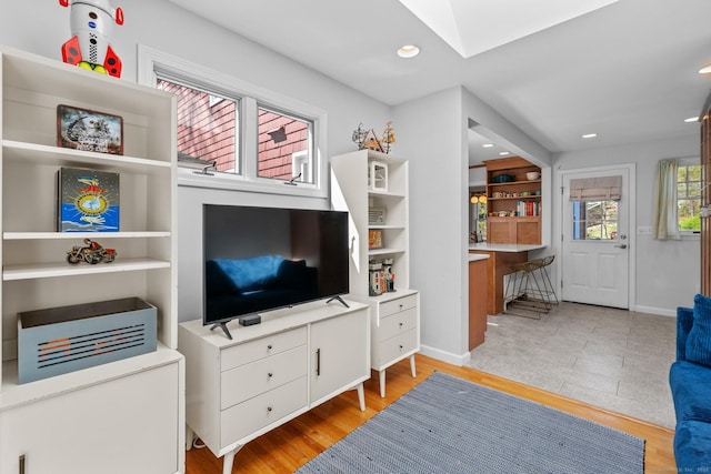 living area featuring a skylight, baseboards, light wood finished floors, and recessed lighting