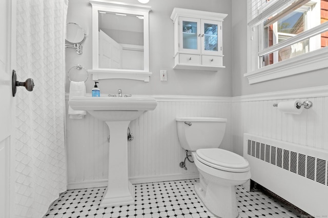 bathroom with radiator heating unit, baseboards, a wainscoted wall, and toilet