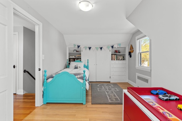 bedroom with radiator heating unit, baseboards, vaulted ceiling, and light wood-style flooring