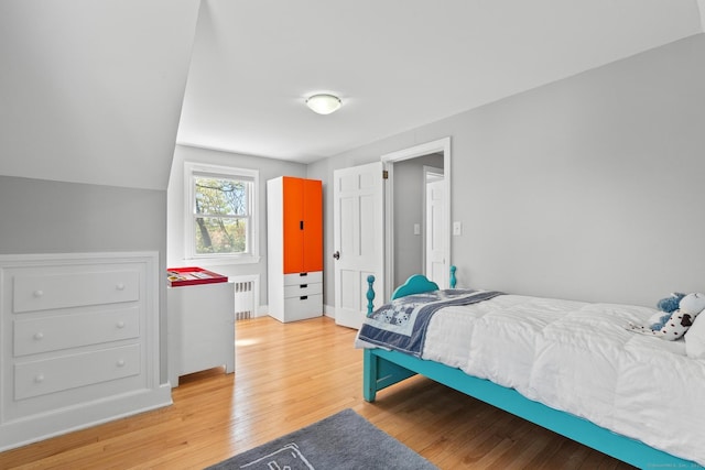 bedroom with baseboards, light wood finished floors, and radiator heating unit