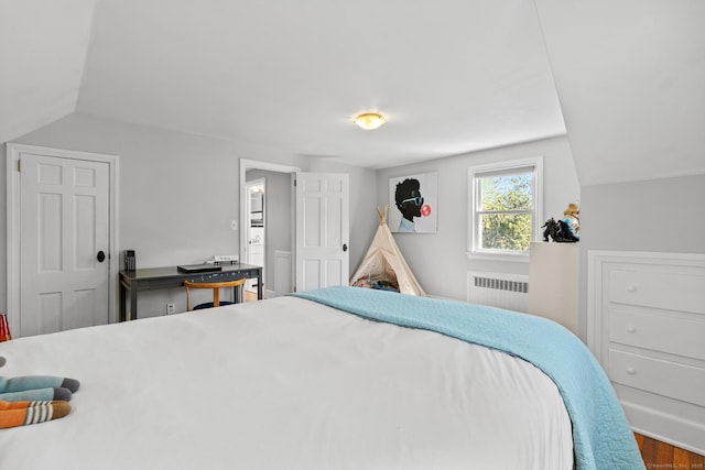 bedroom with radiator, wood finished floors, and vaulted ceiling