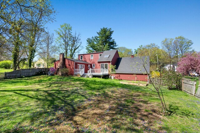 rear view of house with a fenced backyard, a chimney, a lawn, and a deck