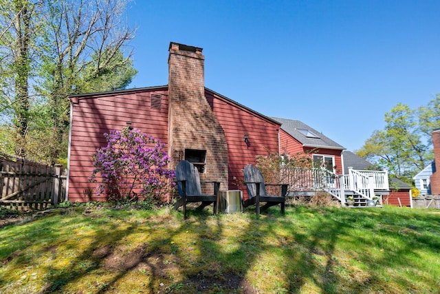 rear view of house with a lawn, a deck, fence, and a chimney