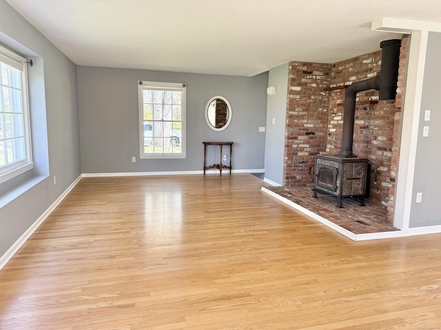 unfurnished living room with baseboards, a wood stove, and light wood-type flooring