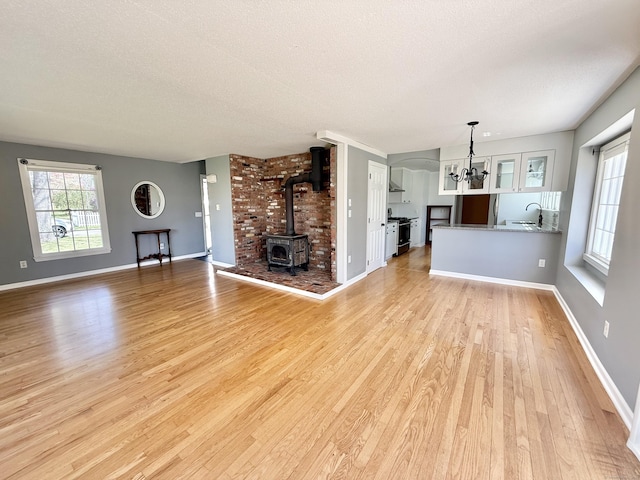 unfurnished living room with a wood stove, baseboards, a textured ceiling, light wood-style flooring, and a notable chandelier