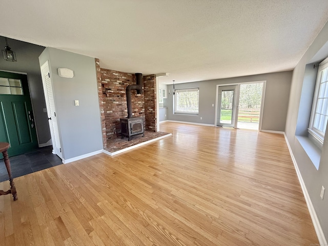 unfurnished living room featuring baseboards, a wood stove, and light wood finished floors