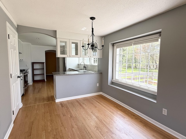 kitchen featuring white cabinets, a notable chandelier, stainless steel gas range oven, arched walkways, and wood finished floors
