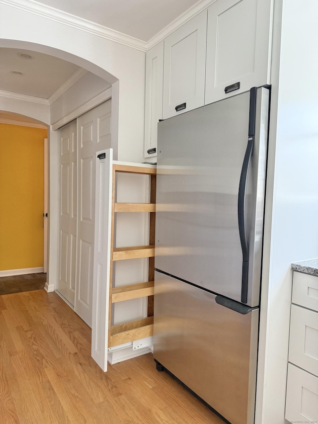 kitchen with arched walkways, light wood-type flooring, white cabinets, freestanding refrigerator, and ornamental molding