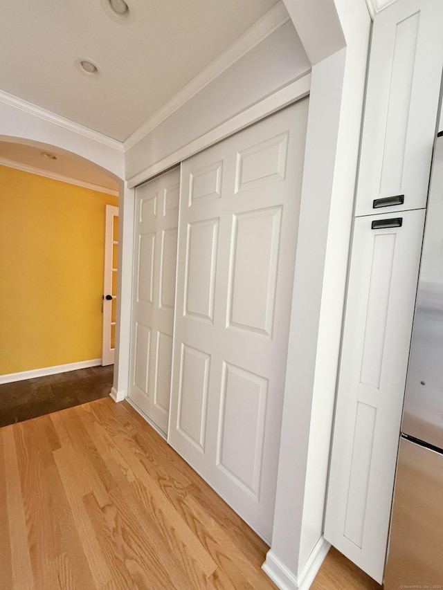 hall with crown molding, arched walkways, baseboards, and wood finished floors