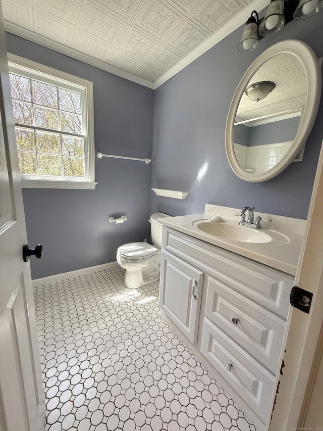 half bathroom featuring vanity, crown molding, toilet, baseboards, and an ornate ceiling