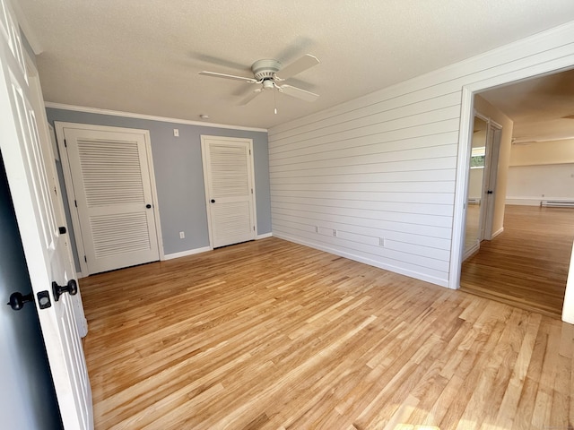 unfurnished bedroom featuring a textured ceiling, multiple closets, baseboards, light wood-type flooring, and ornamental molding