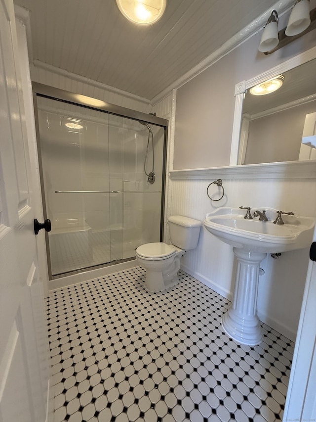 bathroom featuring tile patterned flooring, wainscoting, a shower stall, toilet, and ornamental molding