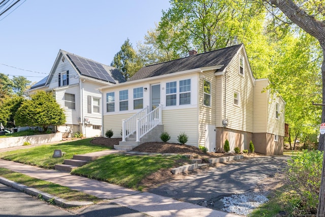view of front of house with entry steps, a chimney, a front yard, and aphalt driveway