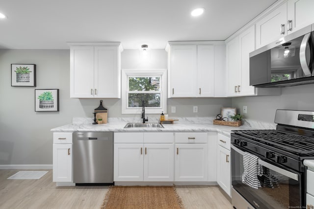 kitchen with white cabinets, a sink, light wood-style floors, stainless steel appliances, and baseboards