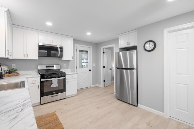 kitchen featuring baseboards, white cabinetry, a sink, light wood finished floors, and appliances with stainless steel finishes