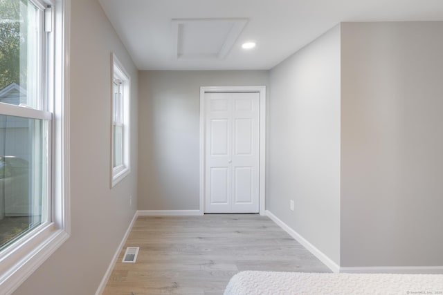unfurnished bedroom with visible vents, attic access, light wood-style floors, and multiple windows