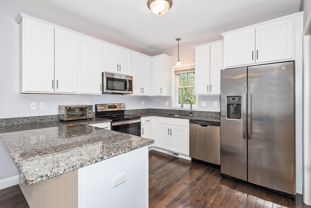 kitchen with appliances with stainless steel finishes, a toaster, a sink, a peninsula, and dark stone counters