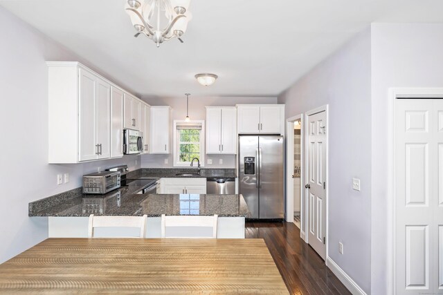 kitchen featuring a sink, white cabinets, a peninsula, a notable chandelier, and stainless steel appliances