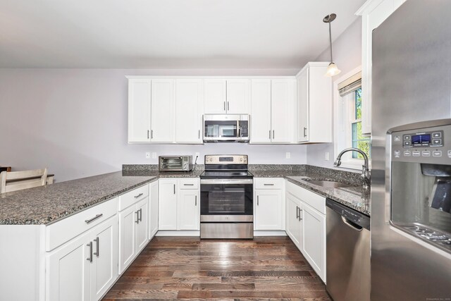 kitchen with a sink, white cabinets, dark stone countertops, a peninsula, and stainless steel appliances
