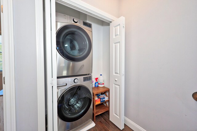 washroom with baseboards, stacked washer and clothes dryer, dark wood-type flooring, and laundry area